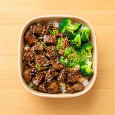 Square bowl of glazed beef and broccoli over rice on a wooden table
