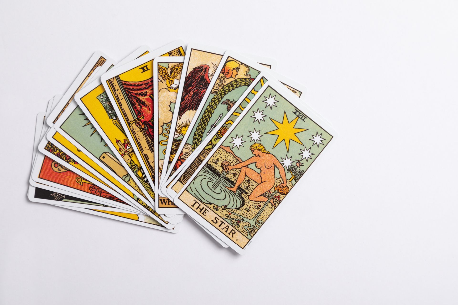 A fan of Tarot cards on a white surface, featuring colorful illustrations. One card visible, labeled 