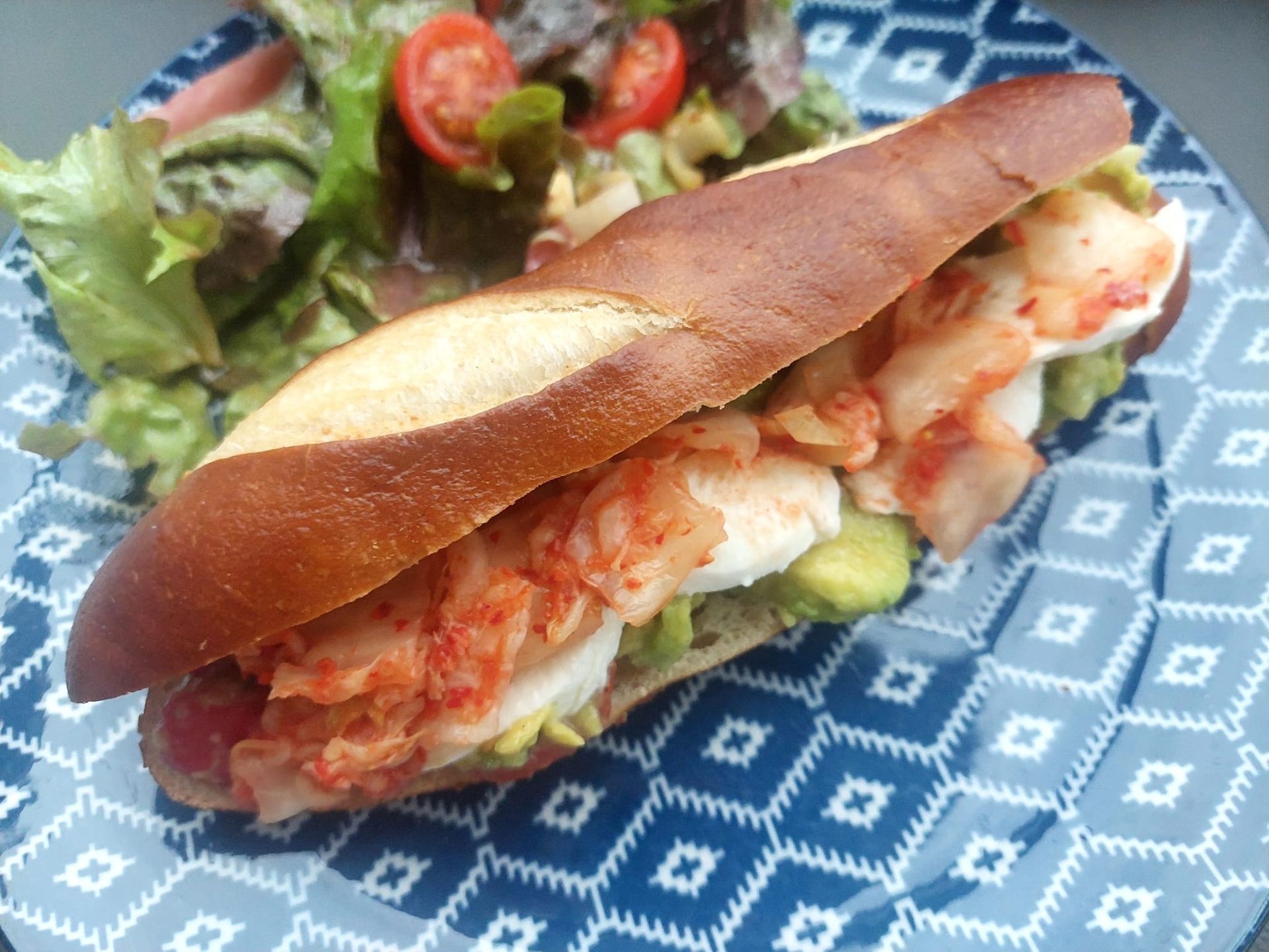 Un sandwich est dans une assiette bleue avec une salade.