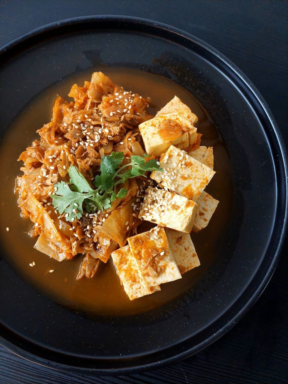 Un bol noir rempli de tofu et de légumes sur une table.