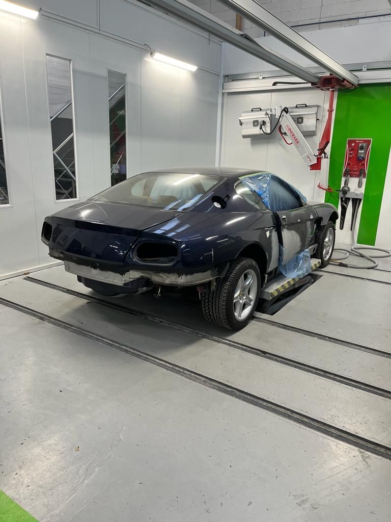 Dark blue sports car in a paint booth, prepared for bodywork.