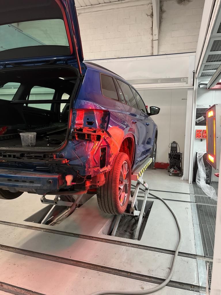 Blue car, rear damage being repaired on a lift in a body shop.