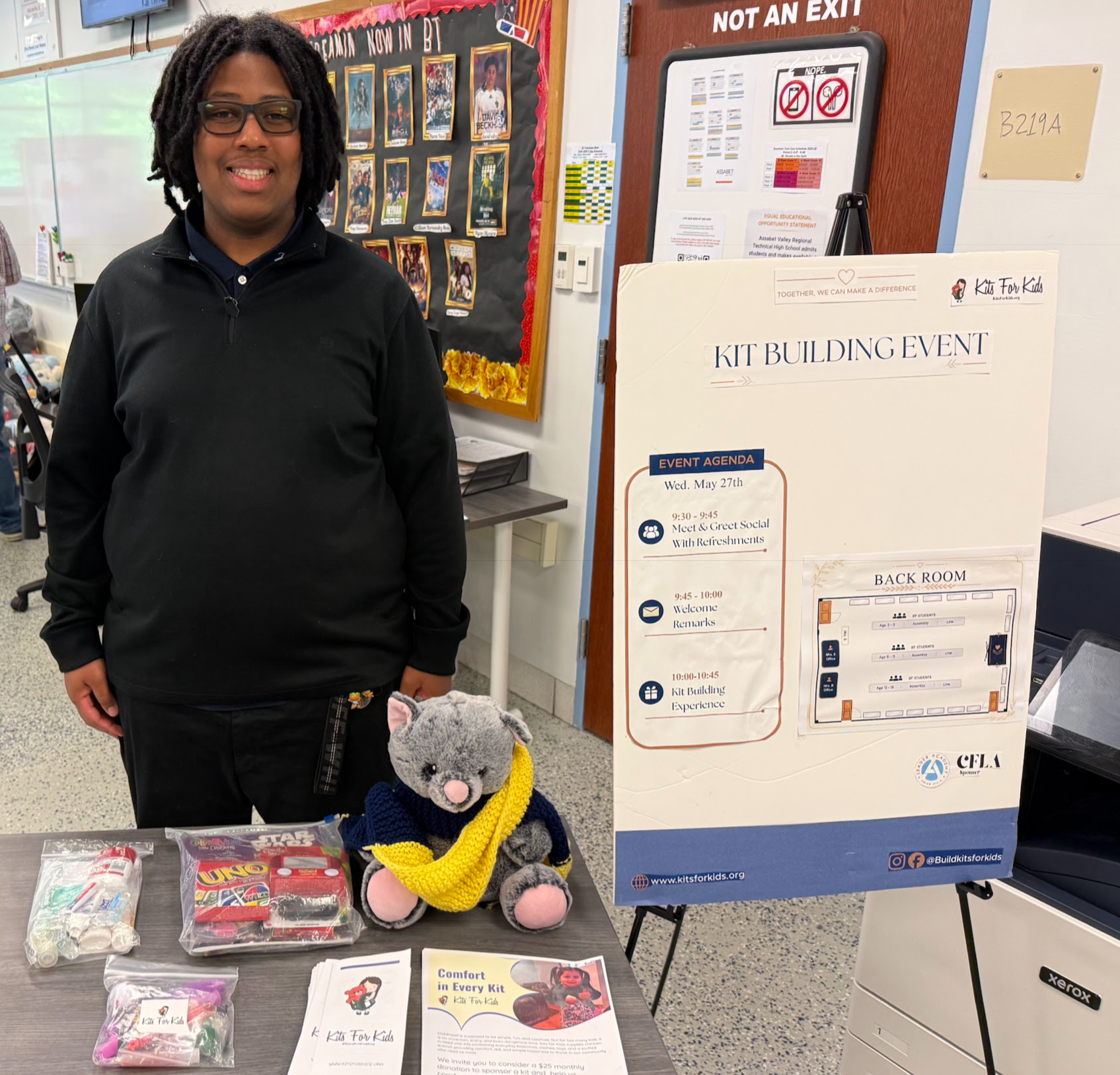 Student standing beside a project display board with stuffed animal and pamphlets on a classroom table