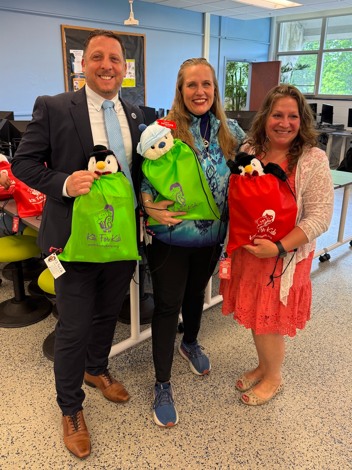 Three people smiling indoors, holding colorful gift bags in a bright room.