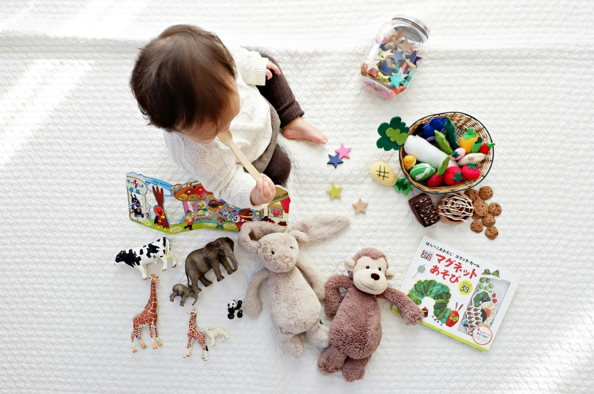 Toddler playing on a white rug with stuffed animals, toys, and a colorful basket nearby