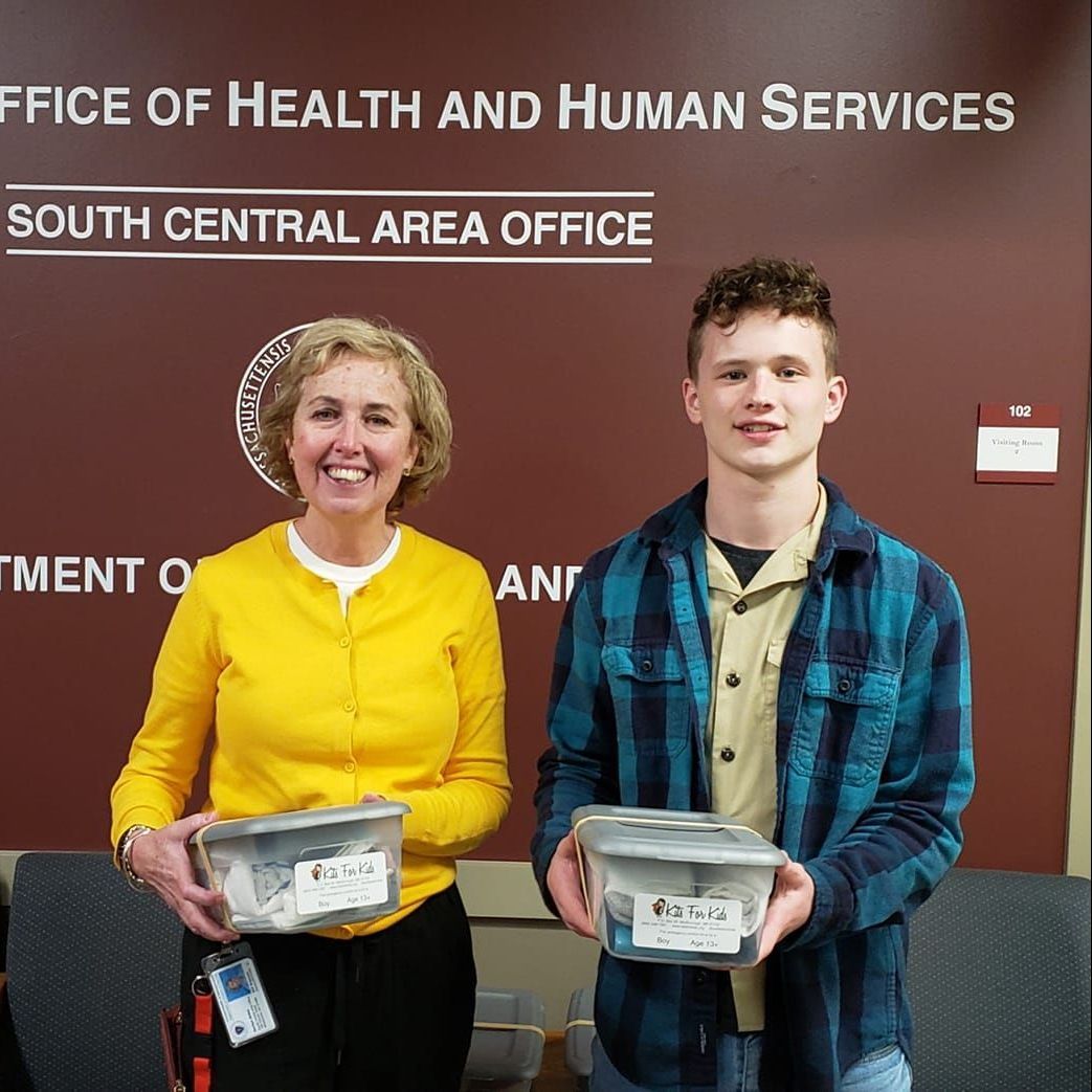 Two people holding food containers in front of a Health and Human Services office sign