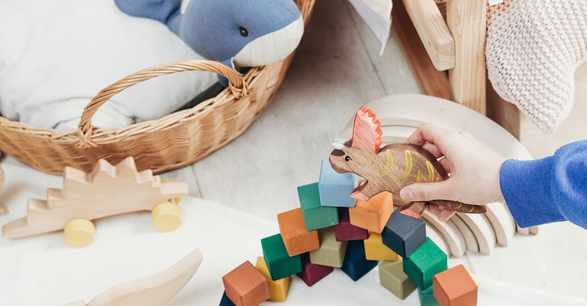 Child’s hands stacking colorful wooden blocks beside a basket and stuffed toy on a play mat