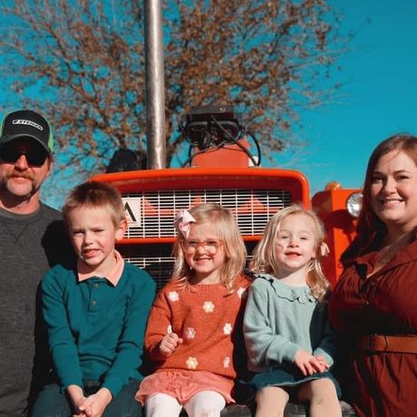 A family is posing for a picture in front of an orange tractor.