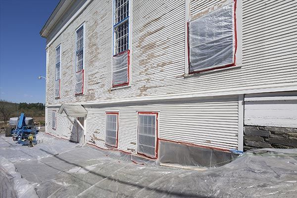 A white building with plastic covering the  Lead Paint windows is being painted.