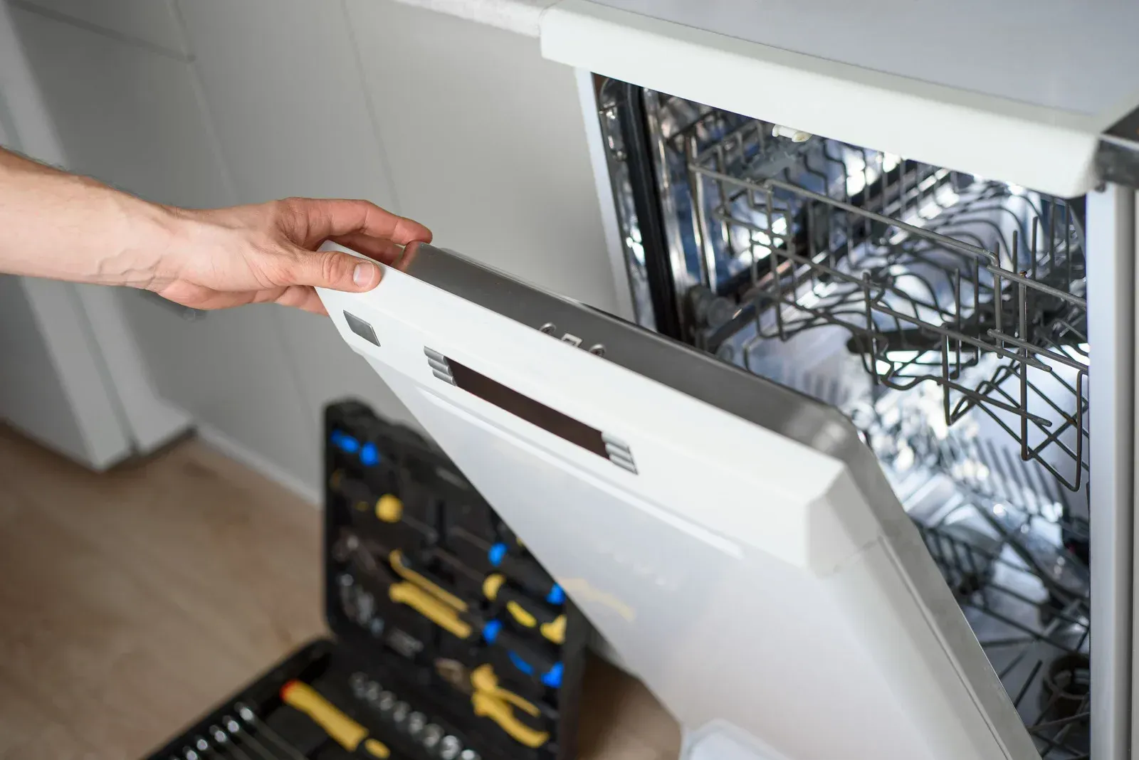 Person opening a dishwasher, toolbox in foreground.