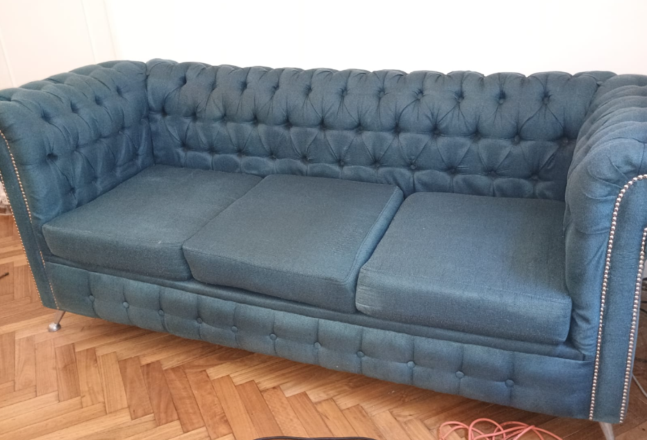 Sofá azul capitoné con detalles de tachuelas plateadas sobre un suelo de madera noble.