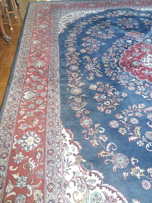 Alfombra con estampado azul y rojo sobre un suelo de madera, que muestra un diseño floral ornamentado.