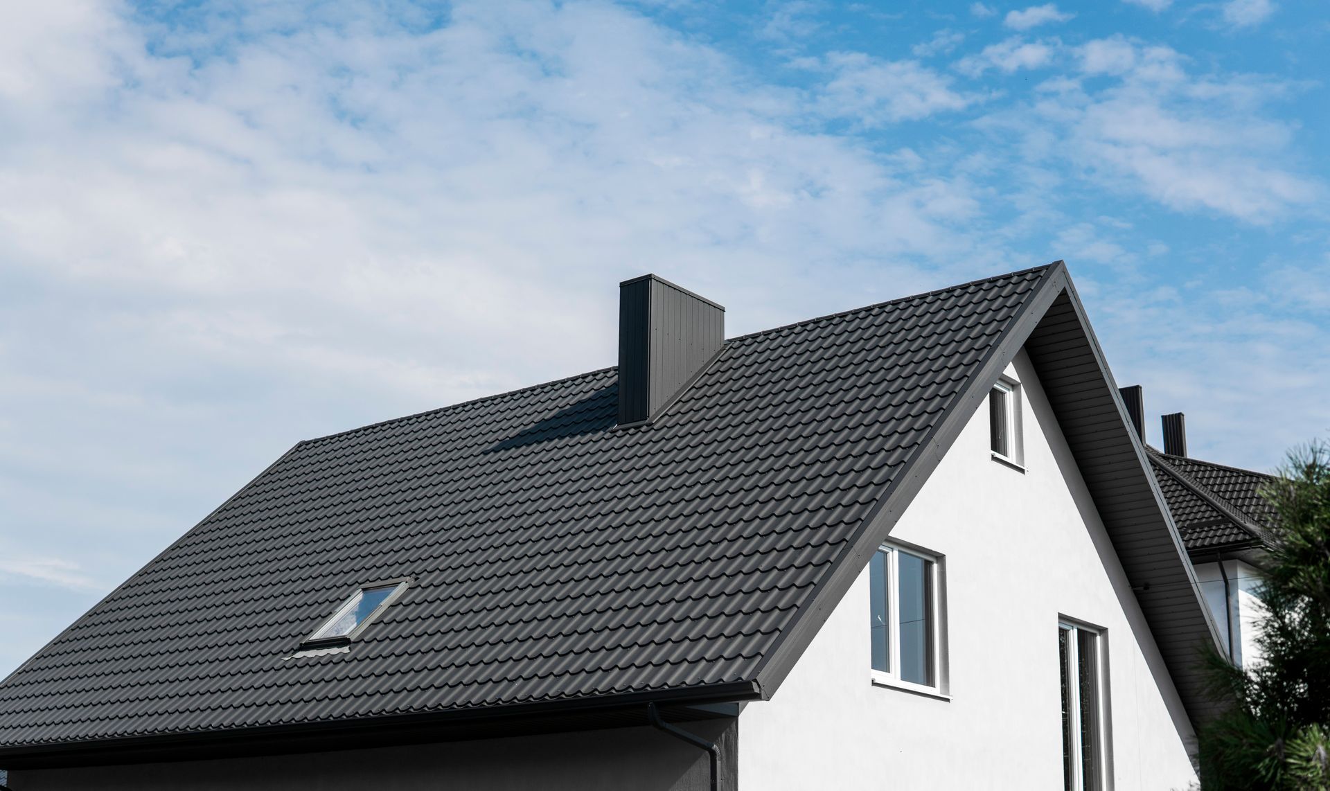 White house with a dark gray tiled roof and skylight against a blue sky