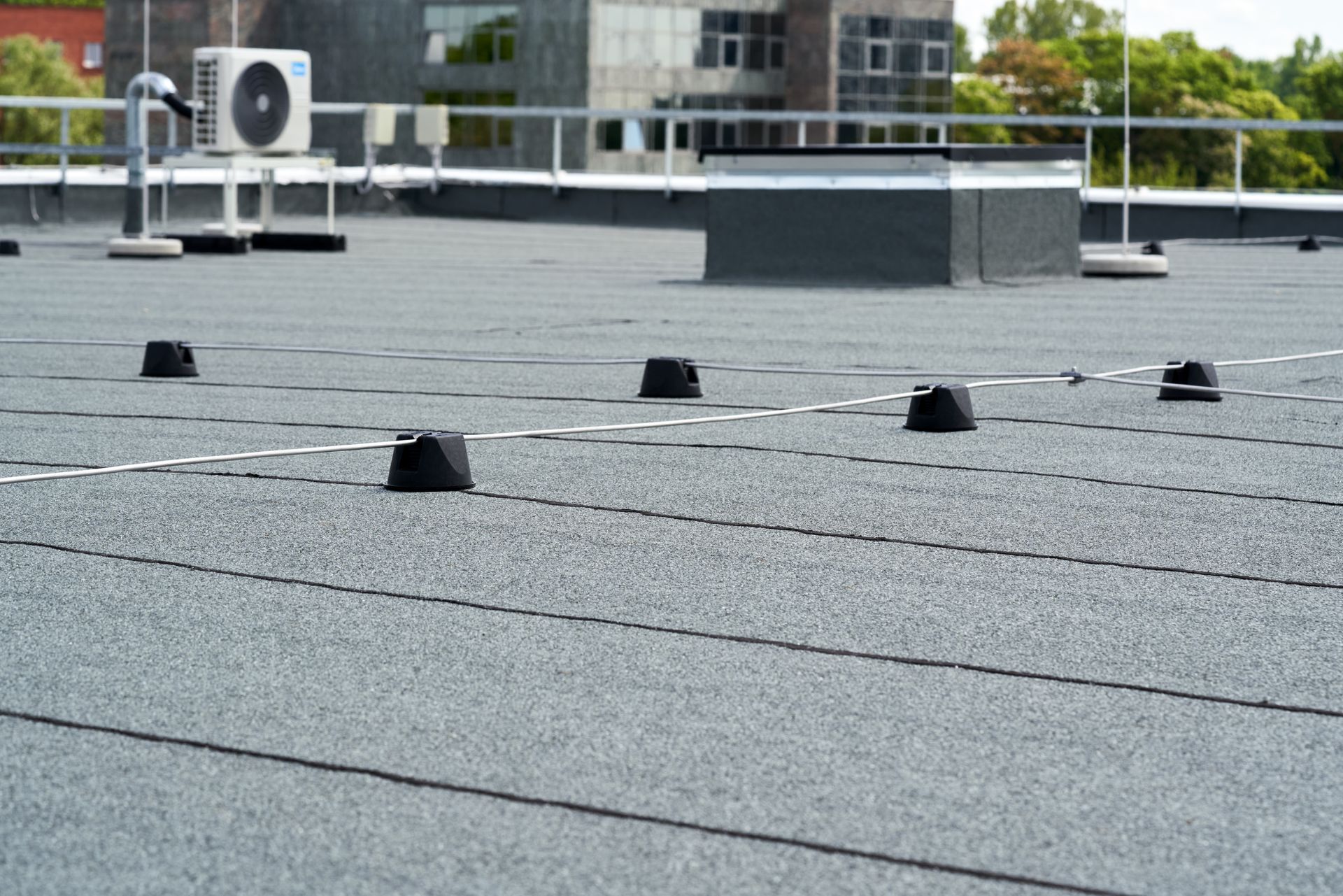 Two construction workers in hard hats install metal roofing panels on a rooftop.