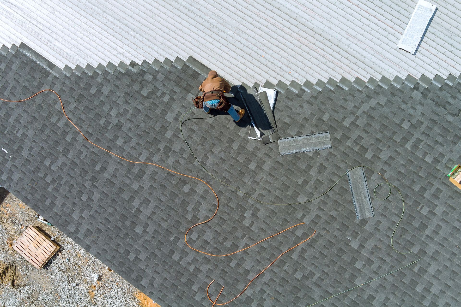 Person in a blue jacket walking on a gray shingled roof beside a white wall.