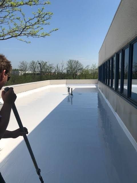 Worker sealing a flat roof seam with a heat tool beside a white parapet wall.