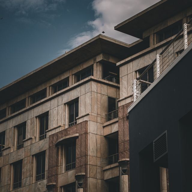 Low-angle view of a beige apartment building with balconies against a cloudy sky