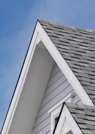 White house gables with gray shingle roof against a blue sky