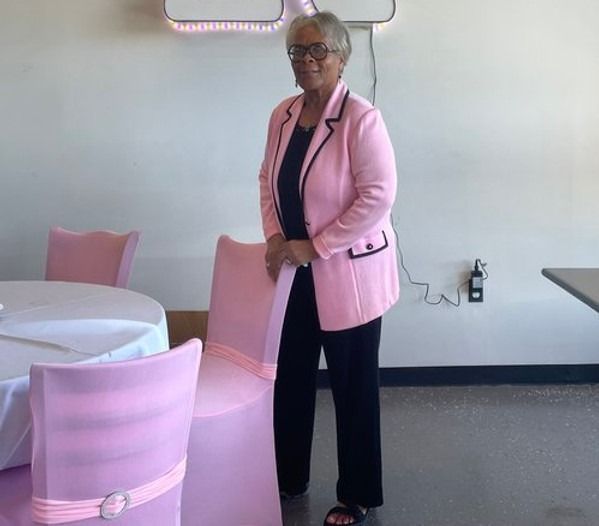 A woman in a pink jacket stands in front of pink chairs