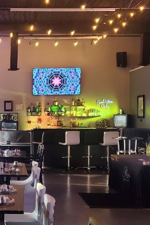A restaurant with tables , chairs , a bar and a large screen on the wall.