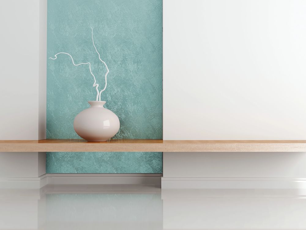 Mensola minimalista con vaso bianco e rami spogli su uno sfondo di pannello testurizzato color verde acqua.