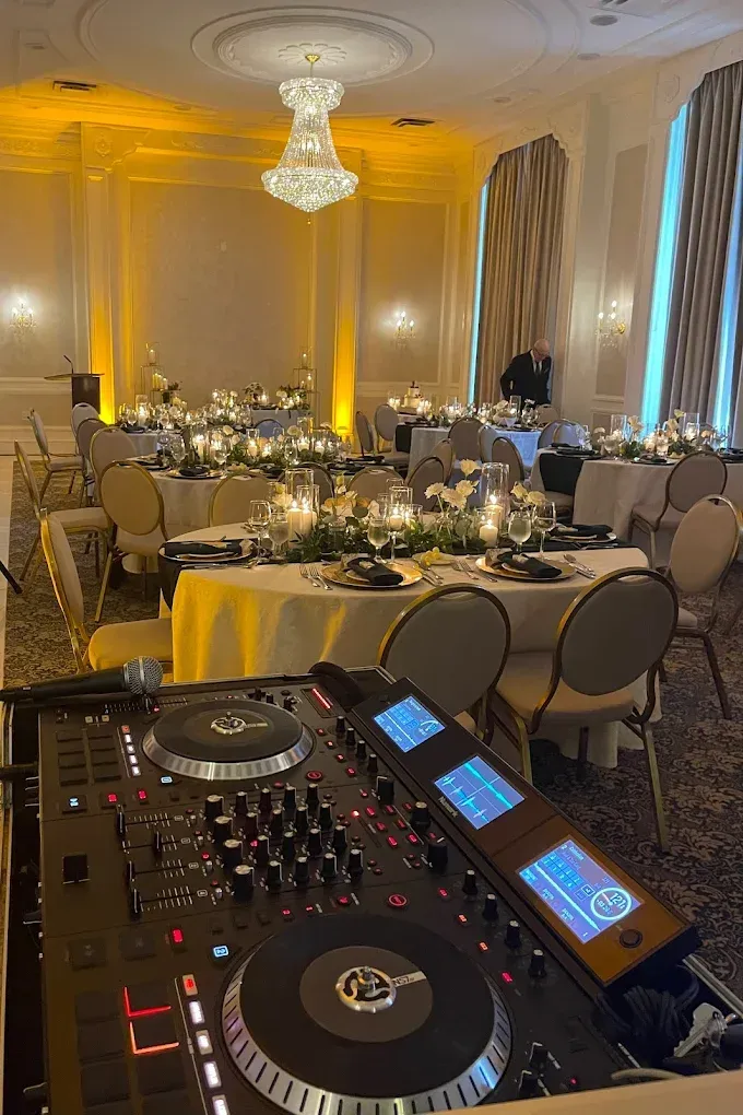 A dj is playing music in a large room with tables and chairs.