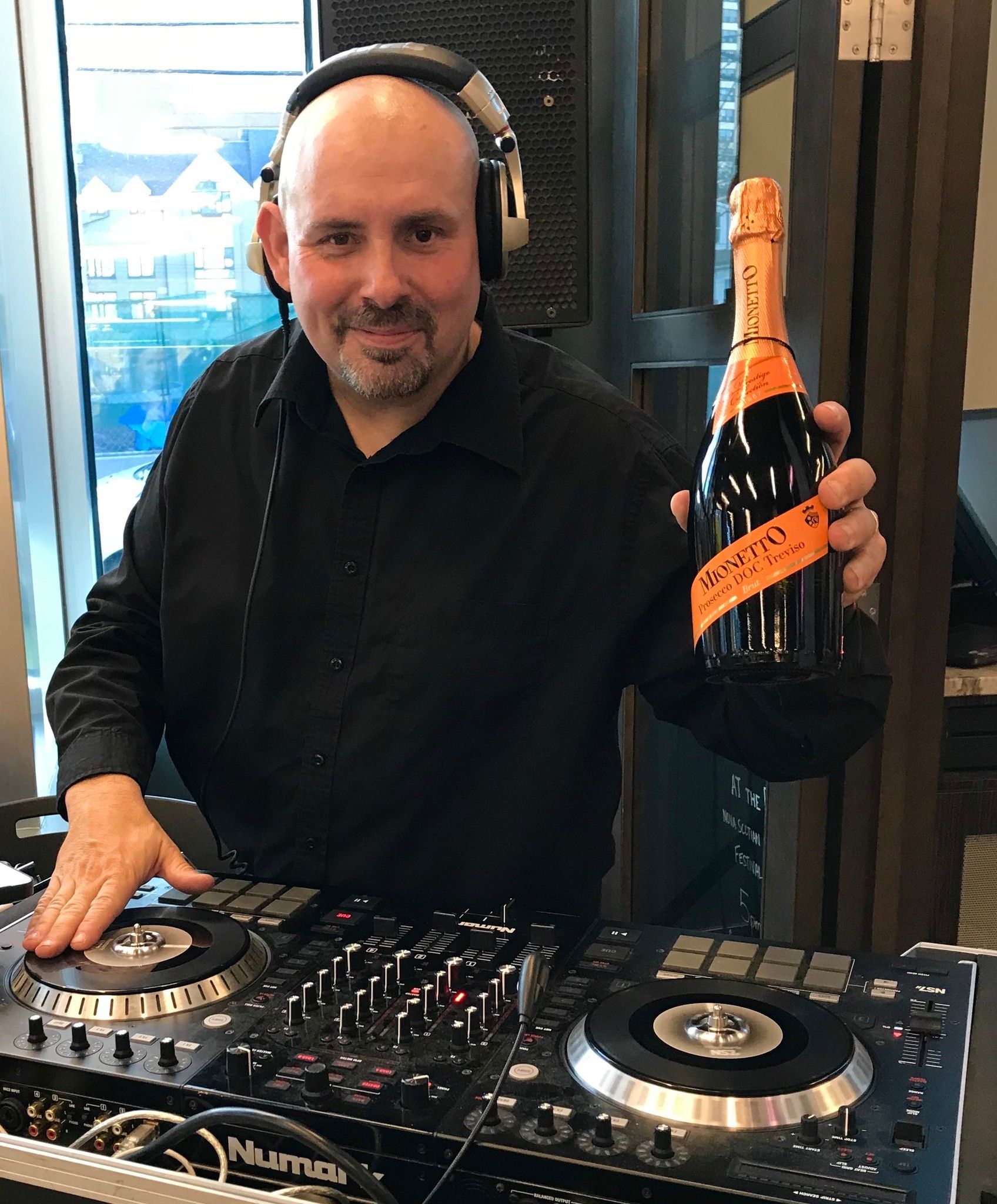 A man wearing headphones is holding a bottle of champagne in front of a dj mixer.