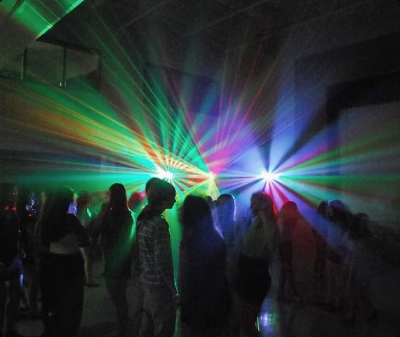 A group of people are dancing in a dark room with colorful lights coming out of the ceiling.