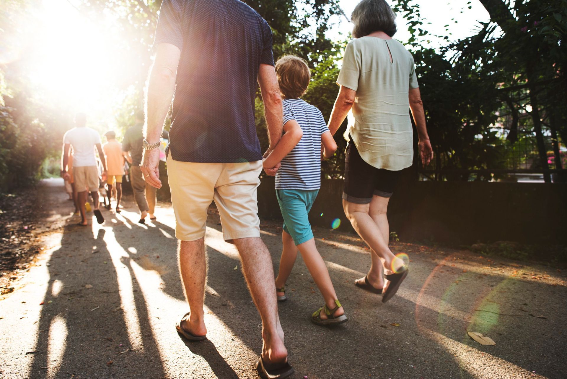 People walking on a sunlit path in a park, with warm light and long shadows