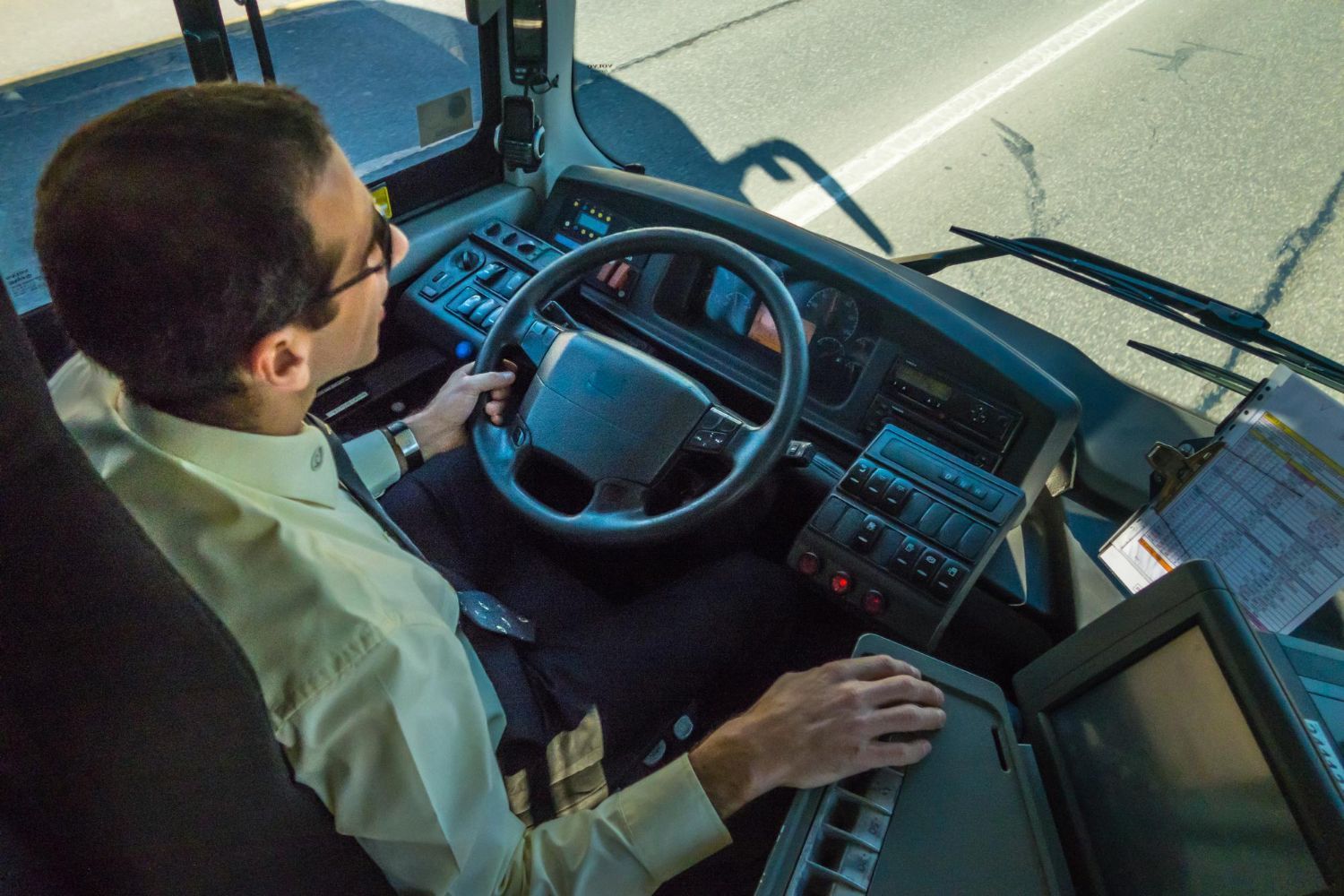 Driver seated at the wheel of a large vehicle, adjusting controls on a road.