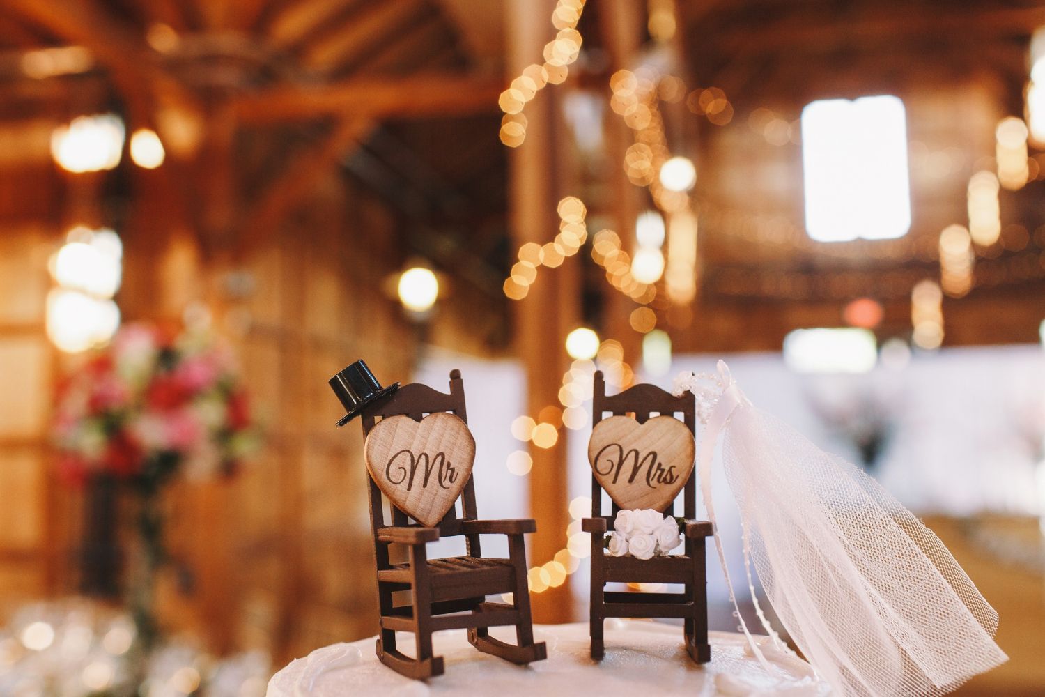 Two small wooden chairs with heart initials and a white veil in a warm, rustic wedding setting