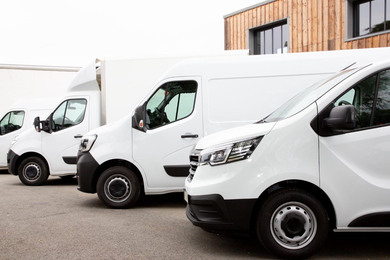 Three white delivery vans parked outside a warehouse