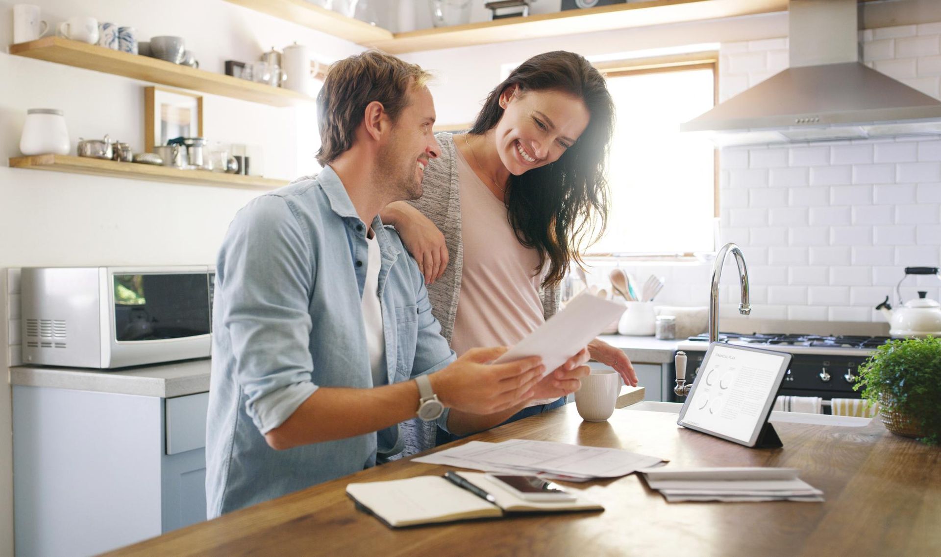 Two people reviewing papers together in a bright kitchen beside a laptop and tablet