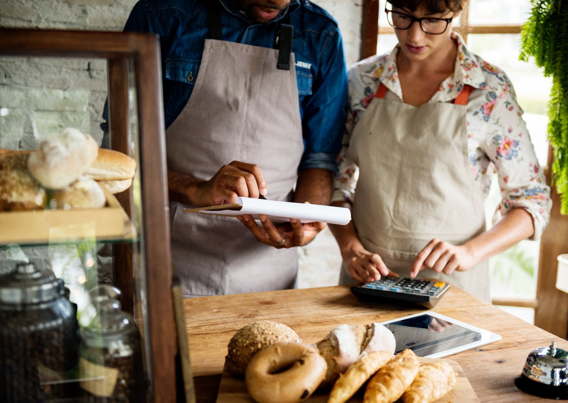 Two bakers in aprons preparing pastries at a wooden counter with bread and ingredients