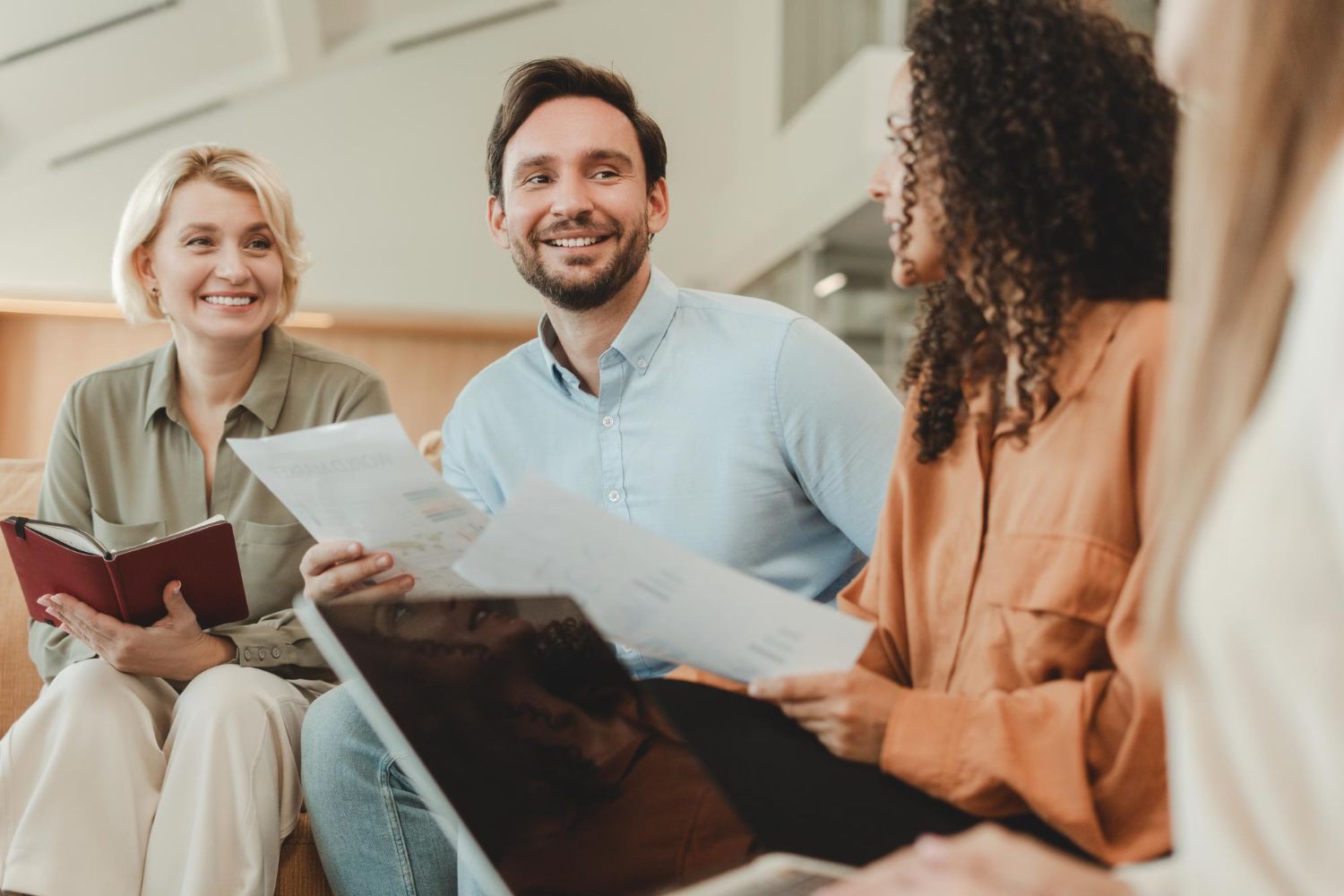 Three people smiling and reviewing papers in a bright office meeting