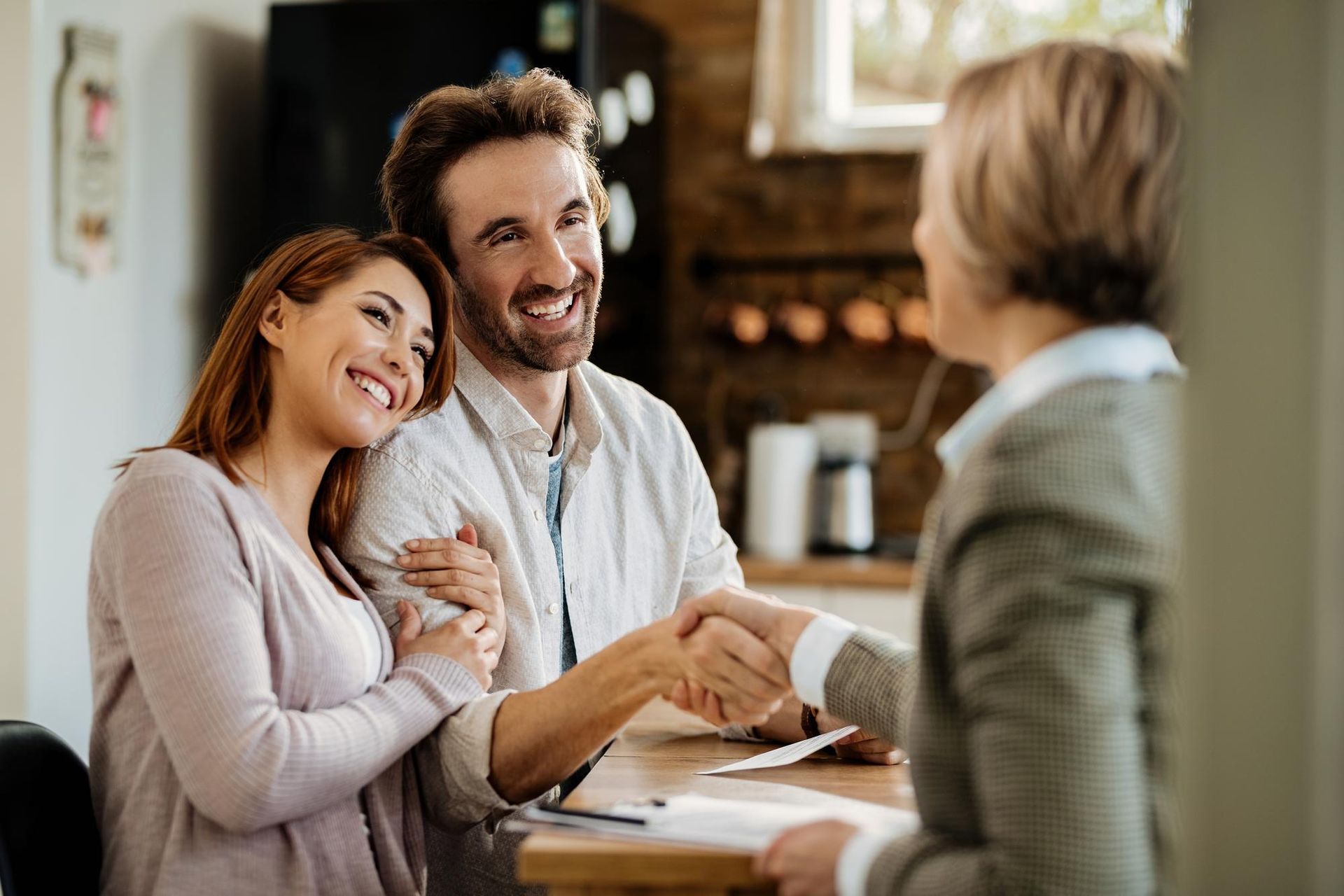 Smiling couple talks with a woman at a table in a cozy kitchen setting