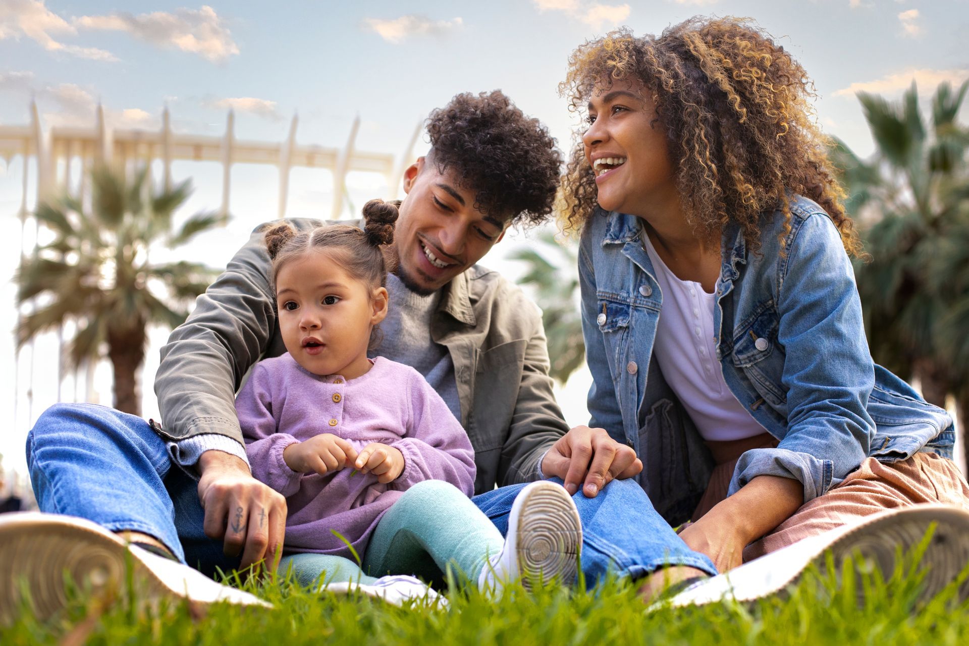 Family sitting on grass outdoors, smiling and relaxing in a sunny park.