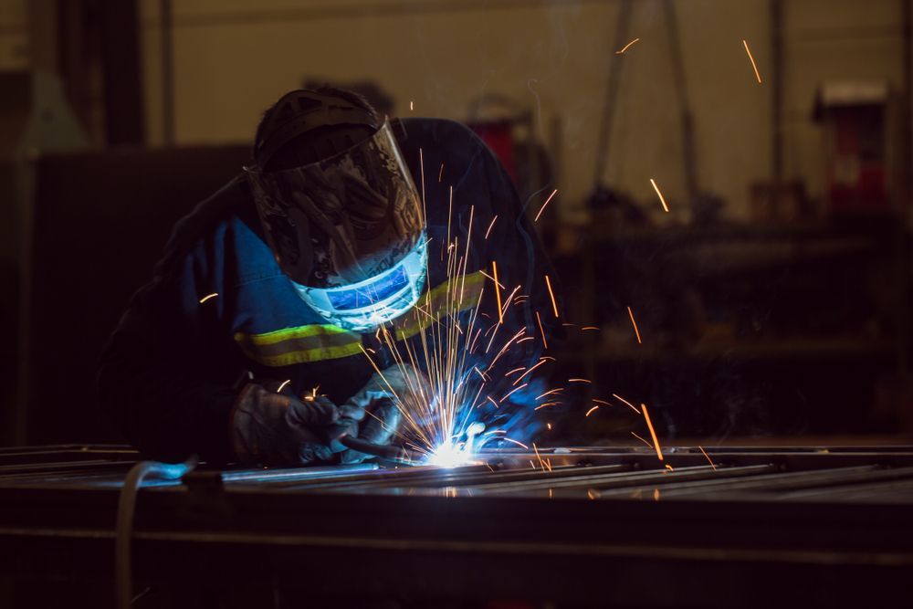 A Man Is Welding A Piece Of Metal In A Dark Room — We Do Fencing in Sunshine Acres, QLD