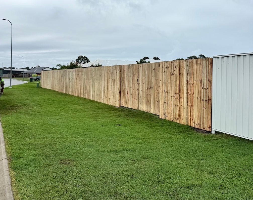 Wooden fence alongside a lawn and road under a cloudy sky— We Do Fencing in Hervey Bay, QLD