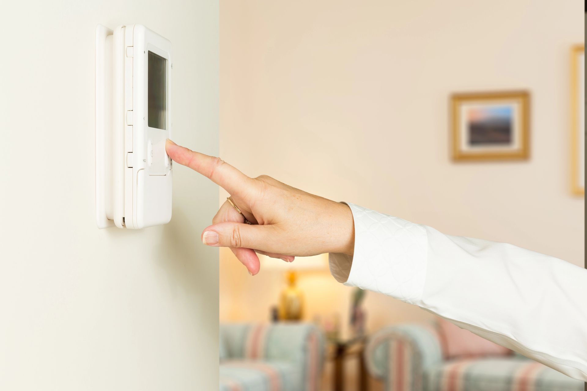 Dito di una persona che preme un pulsante su un termostato bianco montato a parete. Ambiente interno del soggiorno.
