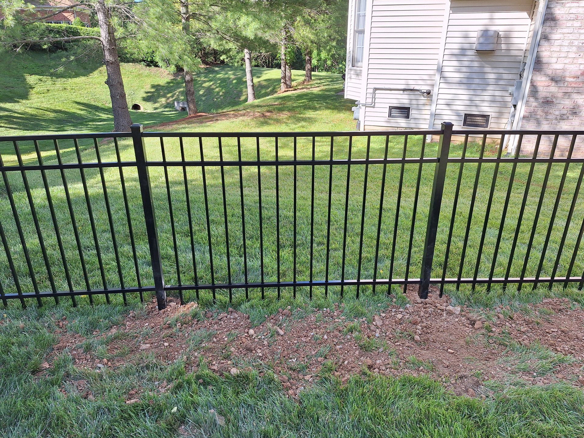Black metal fence in front of a grassy yard, trees, and a white building.