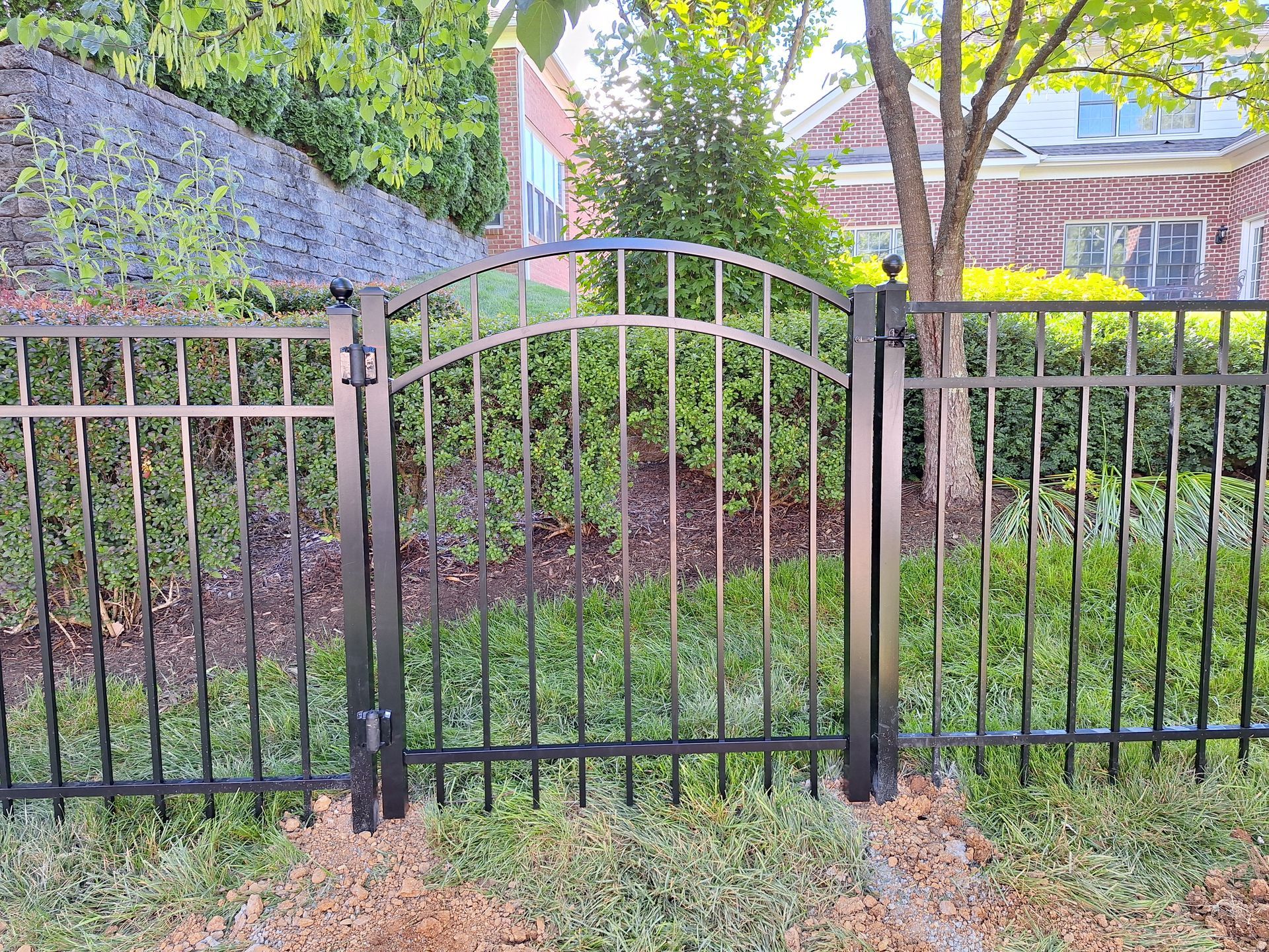 Black metal gate and fence in front of a house with green bushes and grass.