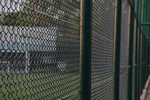 Green chain-link fence outdoors with blurred natural background.