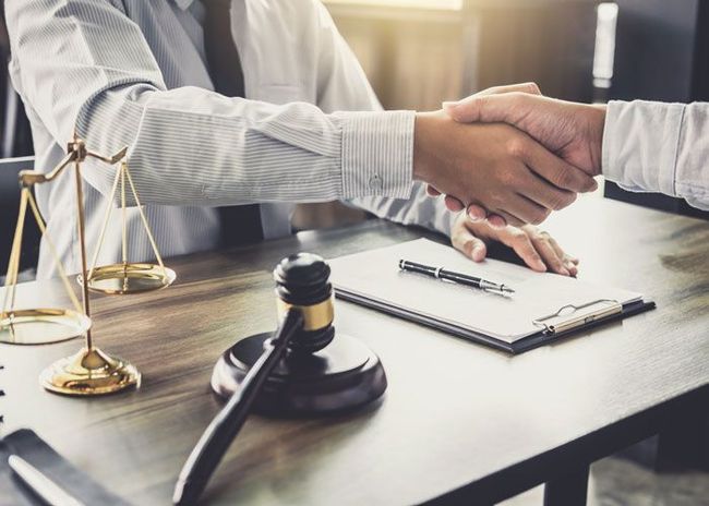 Handshake between two people at a desk with a gavel and legal documents, suggesting a business agreement.