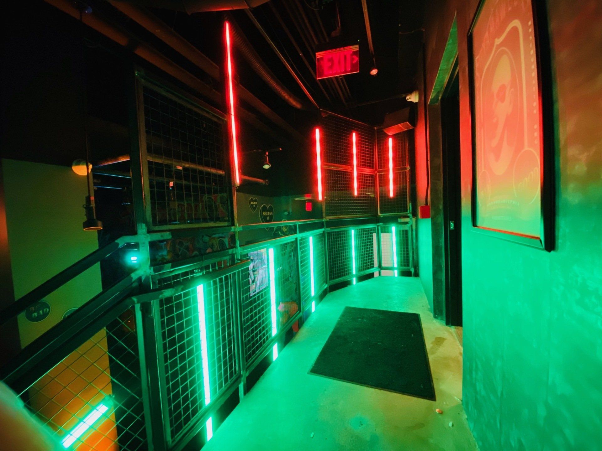 A dark hallway with green lights and a red exit sign.