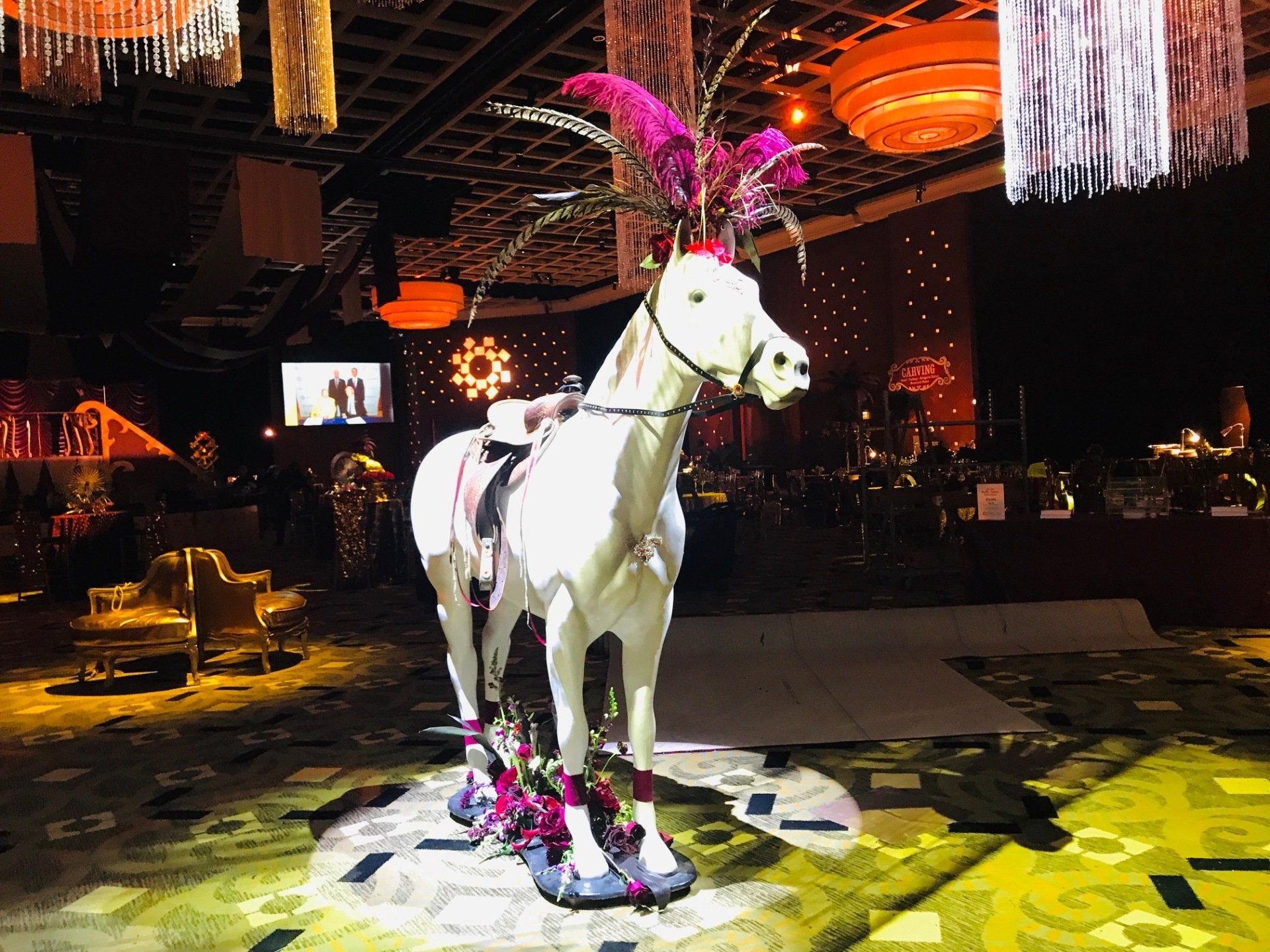A white horse with pink feathers on its head is standing in a room.