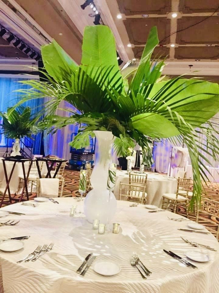 A table set for a wedding reception with a vase filled with green leaves.