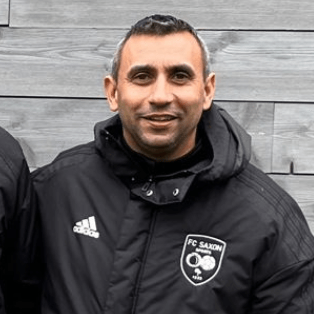 Un homme portant une veste adidas noire se tient devant un mur en bois.