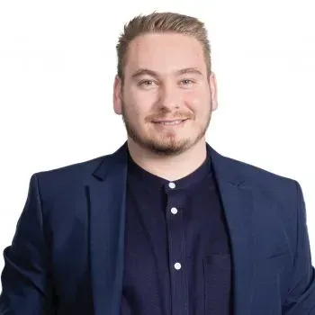 Un homme avec une barbe porte un costume bleu et une chemise noire.