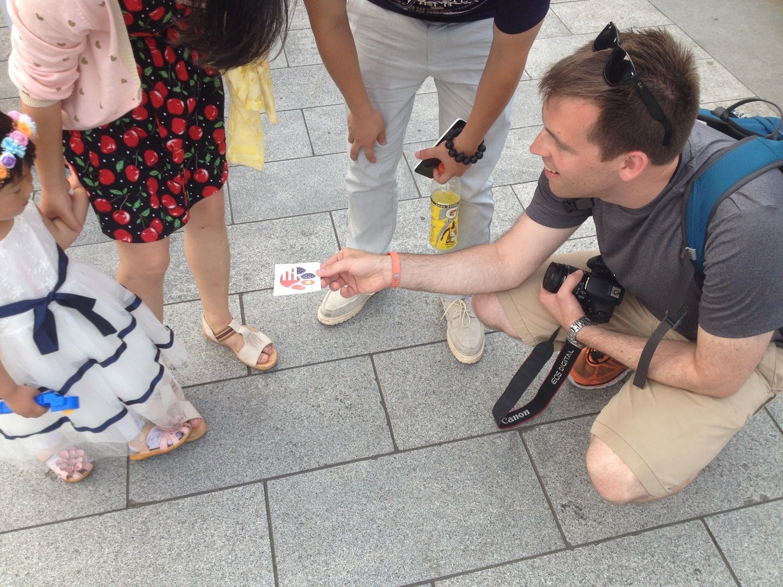 Brian Voss kneels on a sidewalk, handing a small card to two people standing nearby.